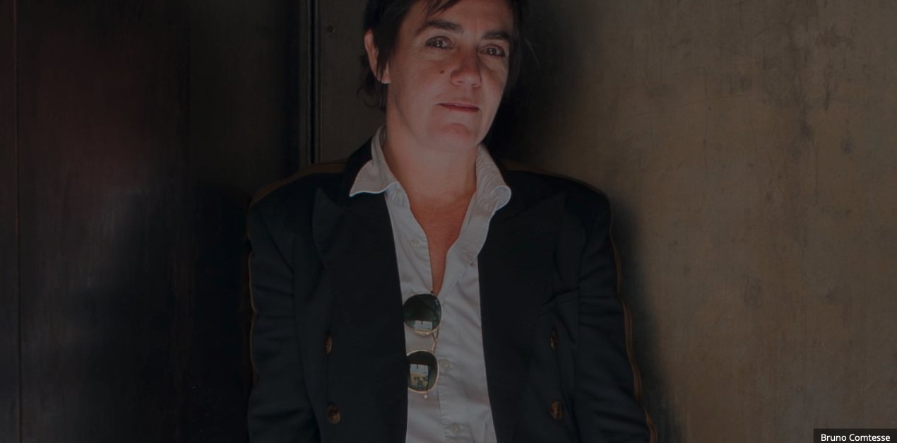 Valérie Texier, en veste sombre et chemise blanche, adossée à un mur clair